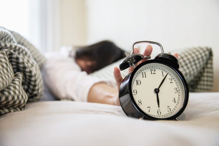 sleepy woman reaching holding alarm clock scaled 1