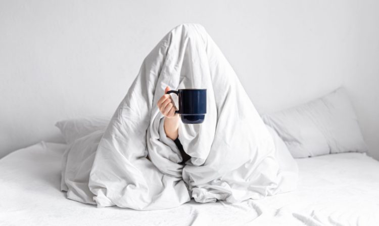 woman wrapped blanket sits bed with cup coffee her hands scaled 1