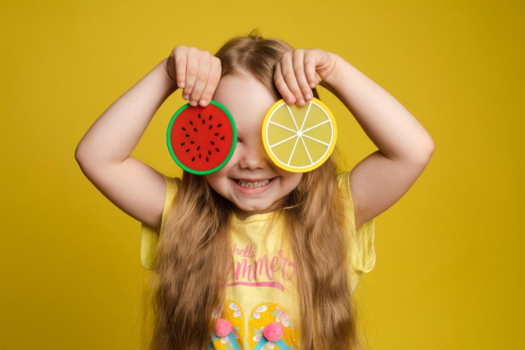 front view happy girl standing yellow isolated background closing eyes with toys cheerful longhaired child laughing playing hide seek concept game happiness